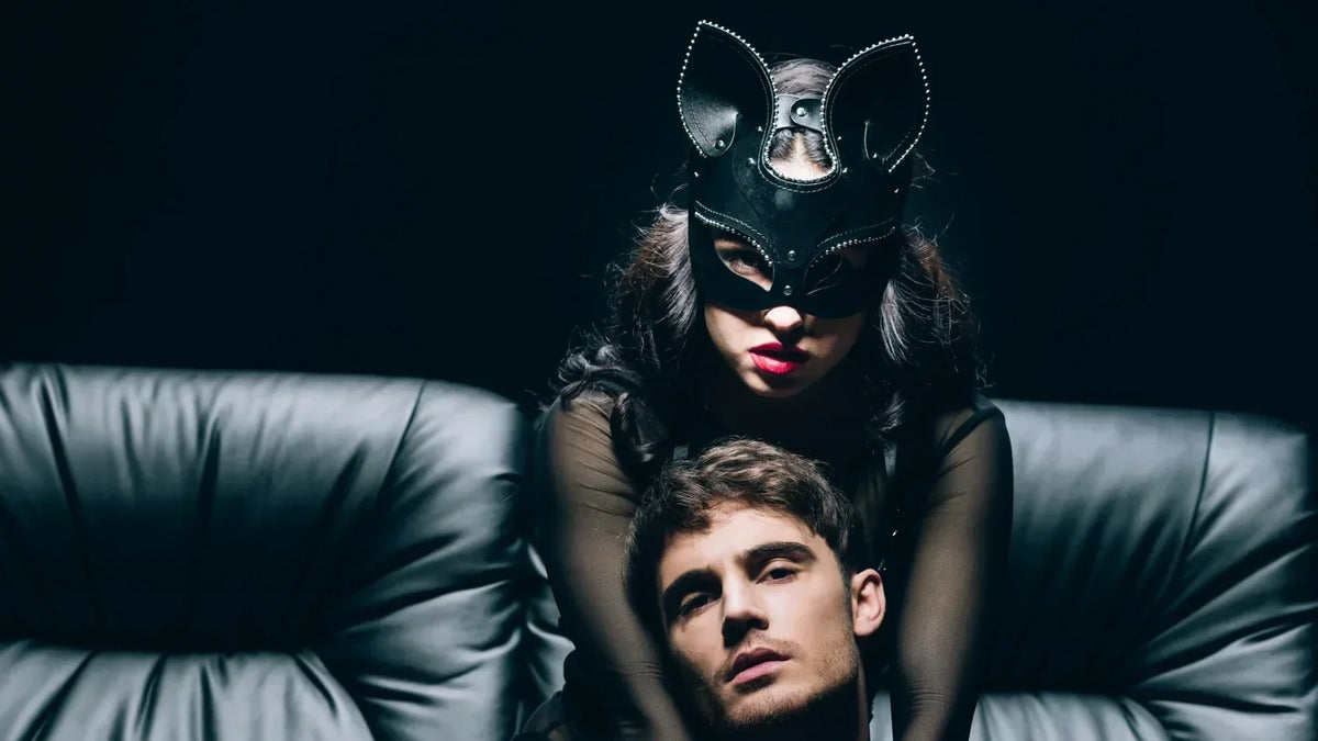 Femme masquée derrière un homme assis sur un canapé, dans une ambiance sombre