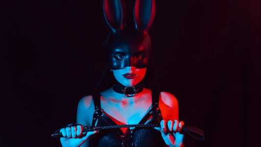 Femme portant un masque noir et tenant une cravache sous un éclairage rouge et bleu